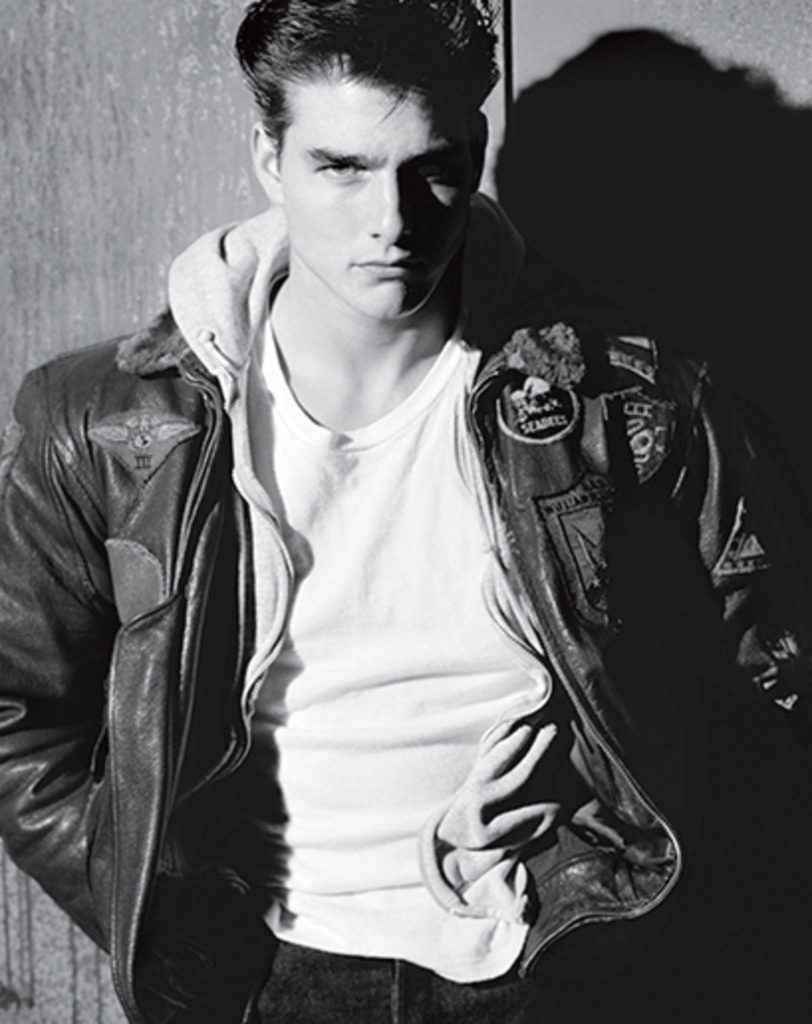 a young Tom Cruise from the 80s posing in a white tshirt and a distressed leather vintage jacket
