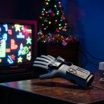 A gray Nintendo Power Glove on a dark table next to an NES and a glowing CRT television.