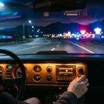 A hand adjusts a cassette player while an empty highway leads toward glowing mountains.