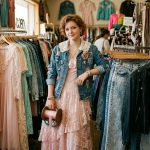 Teen girl in a pink dress holding ribbon inside a vintage clothing shop.