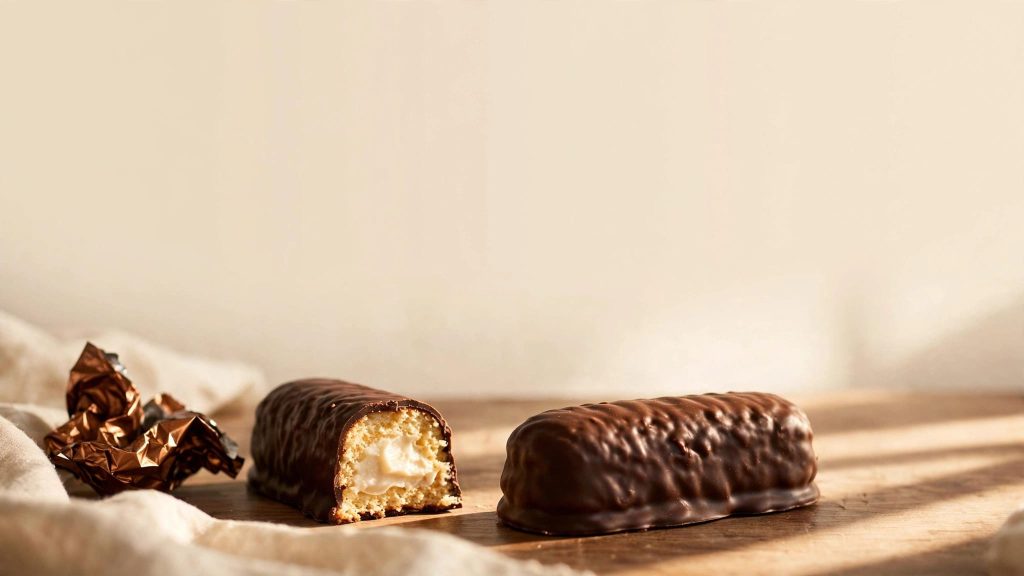 A chocolate-covered snack cake beside a cut piece showing vanilla filling.